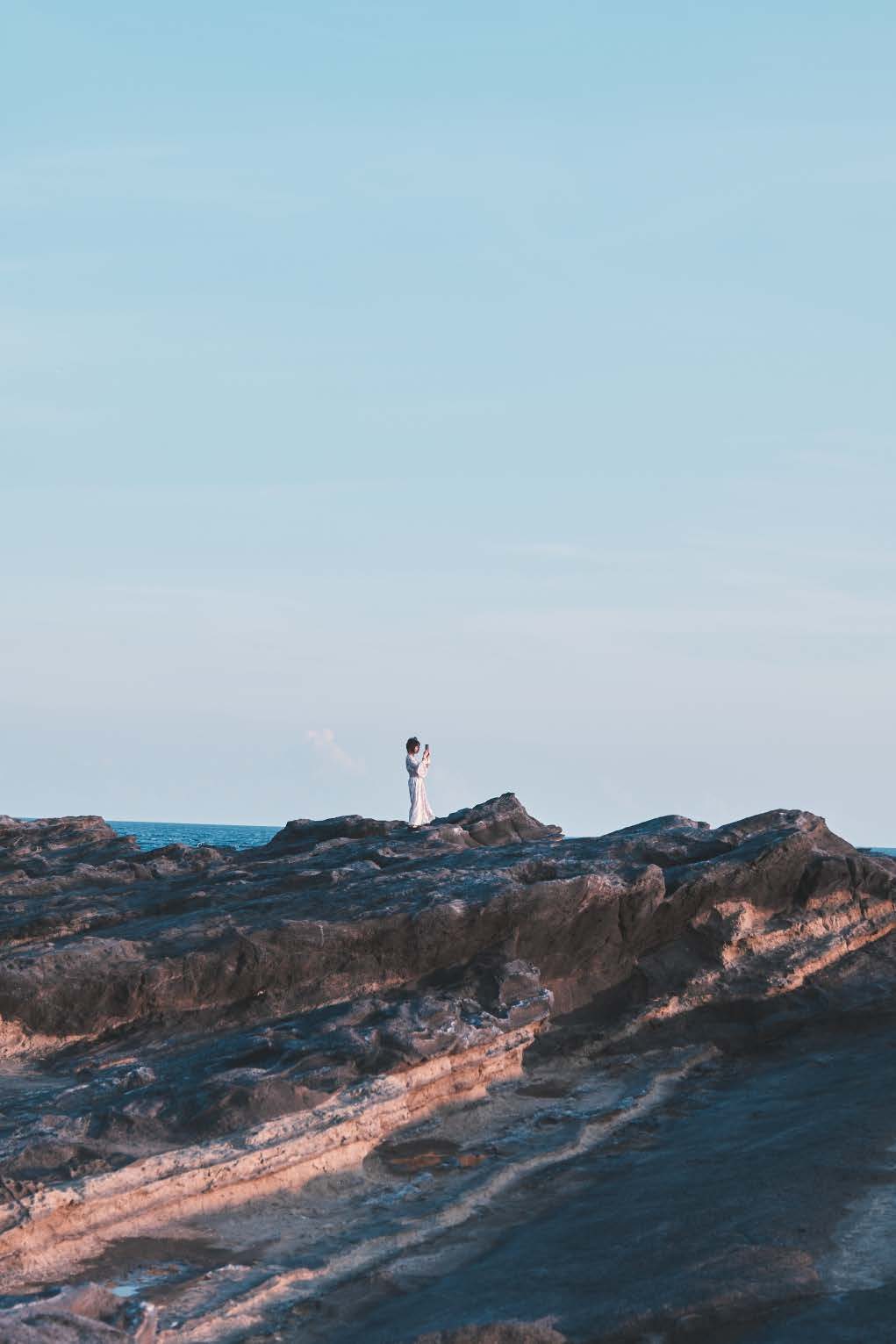 夕方の岩場に立つ人の小さな姿